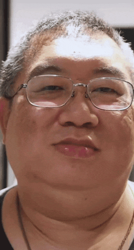a close up of a man 's face with glasses and a necklace