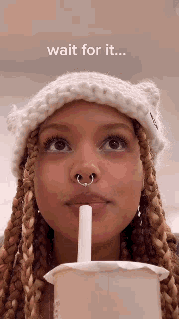 a woman with a nose ring is drinking from a cup with a straw and the words wait for it on the bottom
