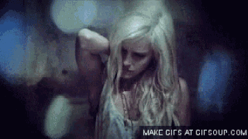 a woman with long blonde hair is standing in a dark room holding her hair .