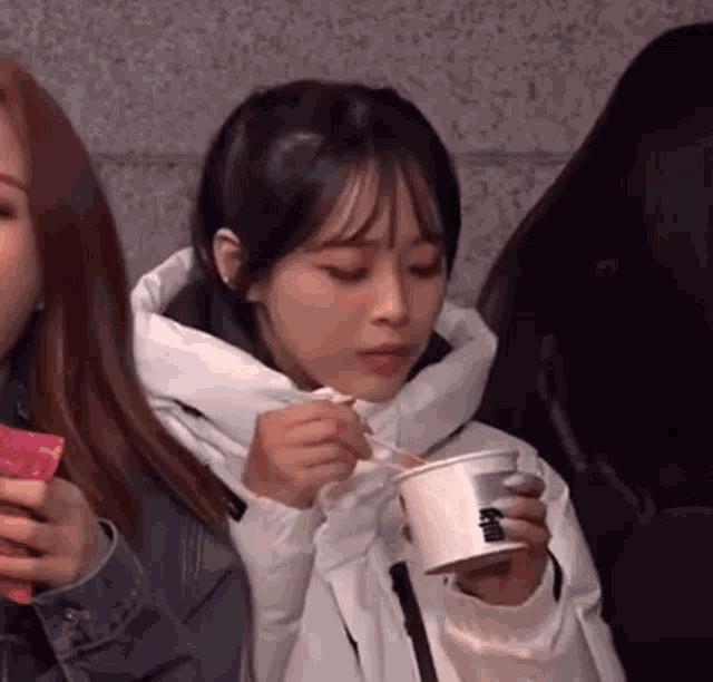 a girl is eating noodles with a spoon from a cup .