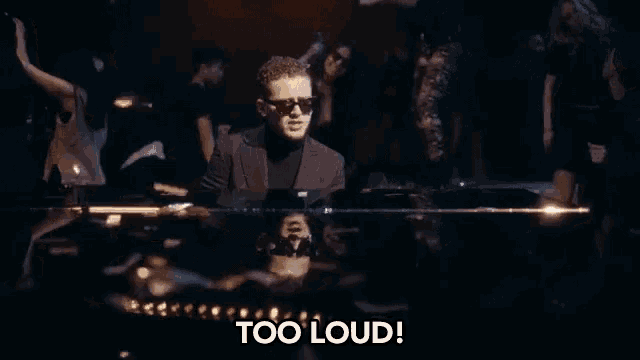 a man in sunglasses is sitting at a piano in front of a crowd of people and says too loud .