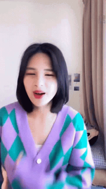 a woman wearing a purple and green sweater is looking at the camera