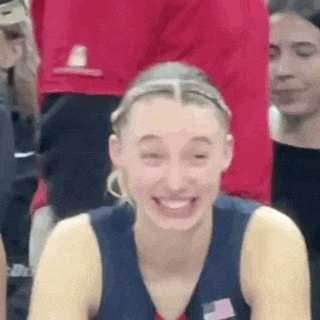 a woman in a basketball uniform is smiling and laughing while sitting in the stands .