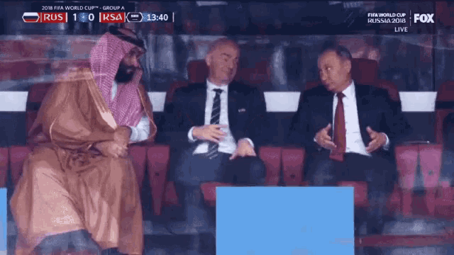 a group of men are sitting in a stadium watching a soccer game and the score is 1-0
