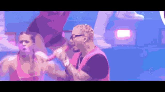 a man in a pink shirt is singing into a microphone while a woman stands behind him
