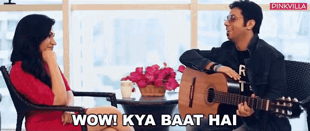 a man is playing a guitar while a woman sits at a table and says wow ! kya baat hai