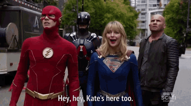 a group of people in superhero costumes are standing on a street and one of them says hey hey kate 's here too