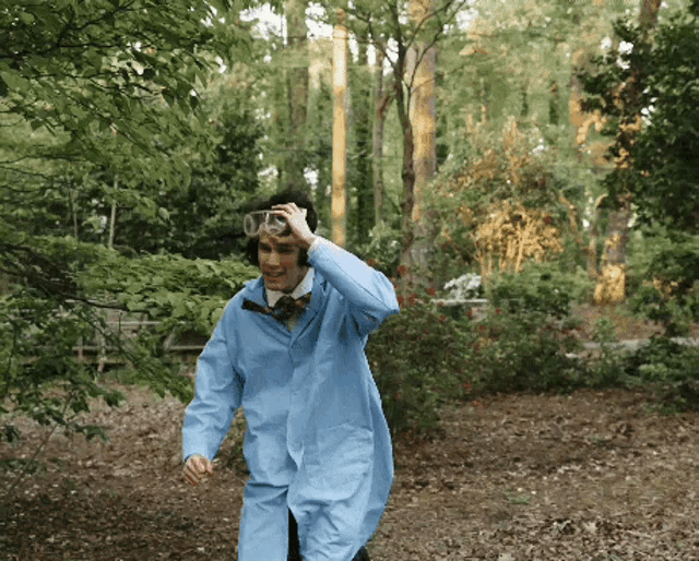 a man in a blue lab coat and goggles is walking through a forest
