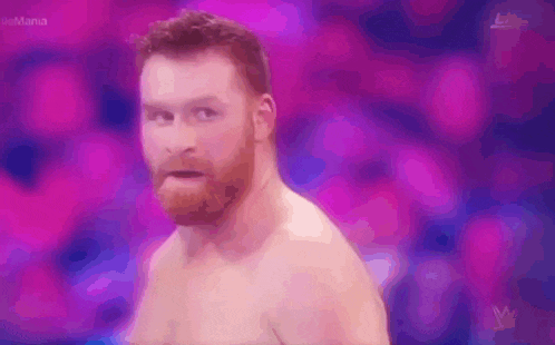 a shirtless man with a beard is standing in front of a pink background .