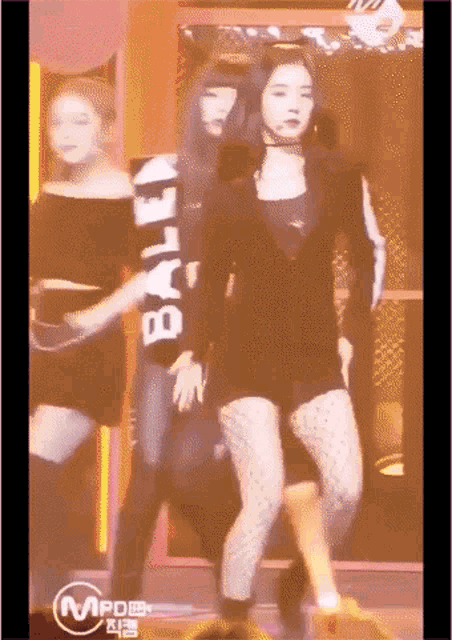 a group of women are dancing on a stage and one of them is wearing a black shirt that says bally