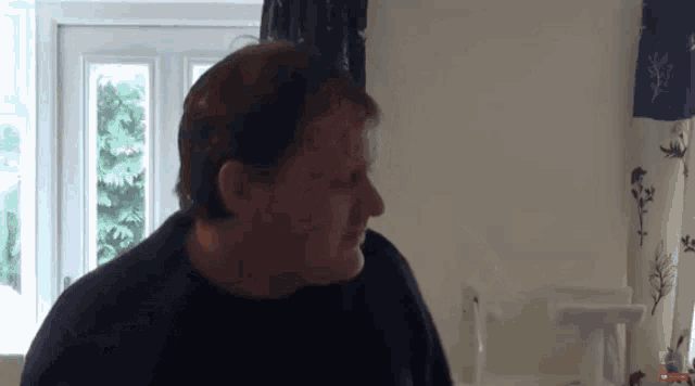 a man in a black shirt is standing in front of a window looking at something