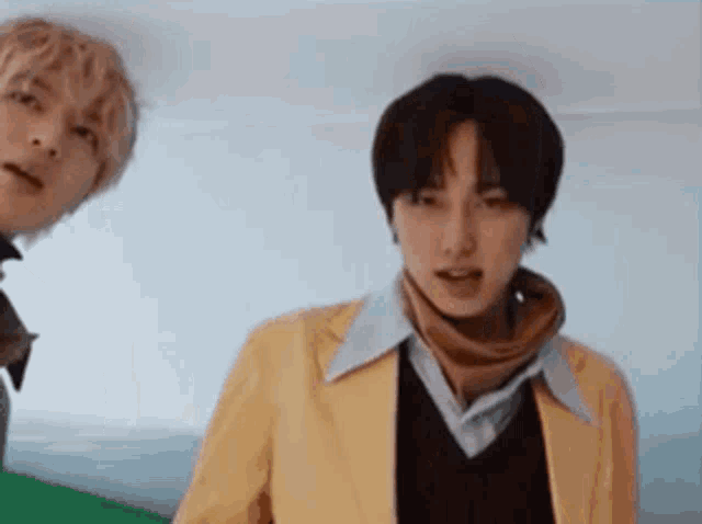 two young men are standing next to each other in a room . one of the men is wearing a yellow jacket .
