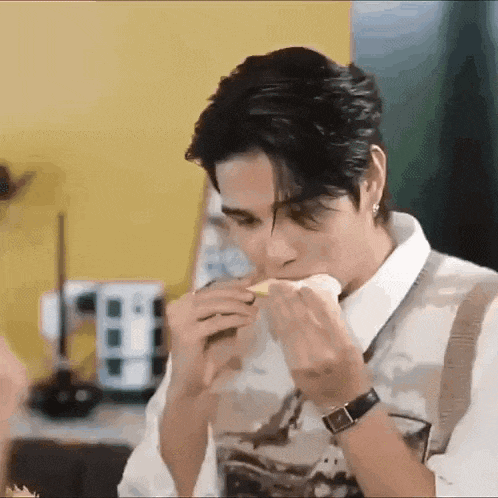 a man is eating a sandwich while wearing a watch and a vest .
