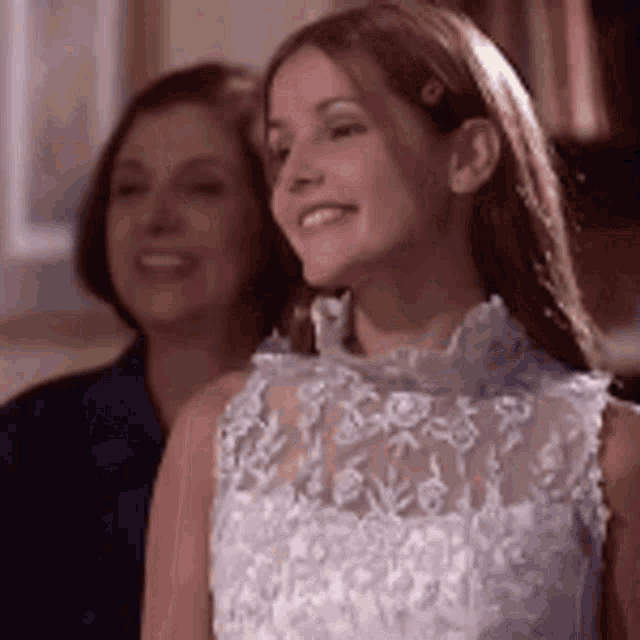 a woman in a white lace dress is smiling in front of another woman