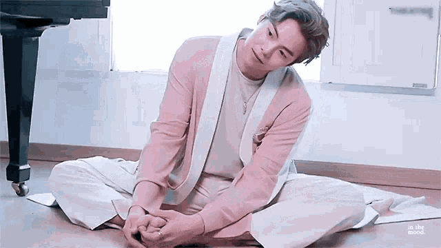 a man in a pink jacket and white pants is sitting on the floor .