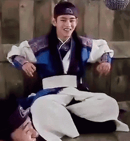 a man in a traditional korean dress is sitting on the floor next to another man .