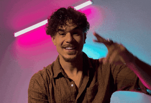 a man with curly hair and a beard is smiling and giving the peace sign