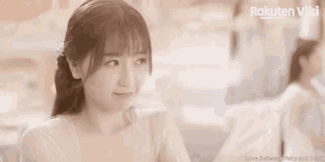 a woman in a white dress is smiling and looking at the camera while sitting at a table .