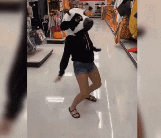 a woman is wearing a panda mask and dancing in a store