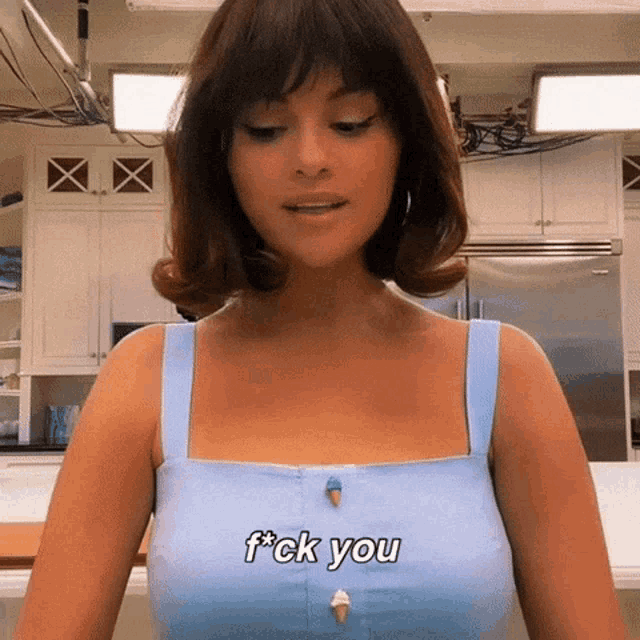 a woman in a blue tank top is standing in a kitchen and says f * ck you