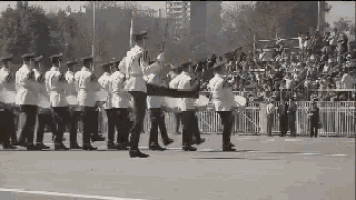 a black and white photo of a military parade with a crowd in the background .