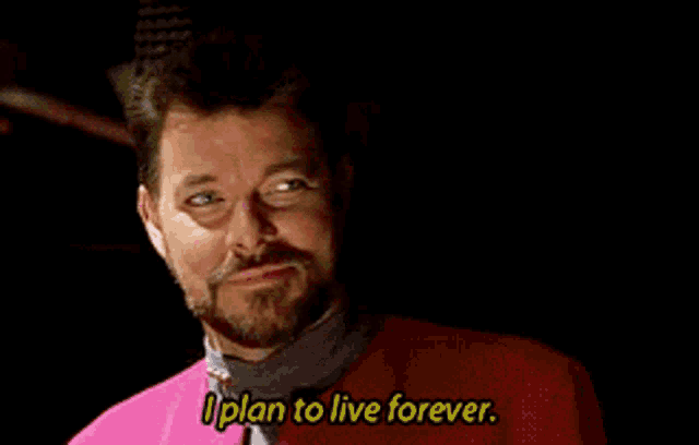 a man with a beard is wearing a pink jacket and says " i plan to live forever "