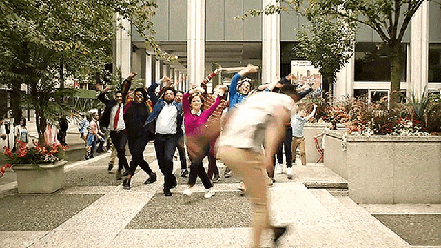 a group of people are dancing on a sidewalk in front of a building .
