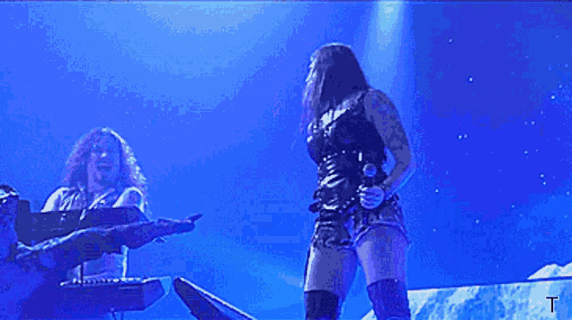 a man playing a keyboard and a woman singing in front of a blue background with the letter t on it