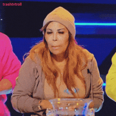 a woman wearing a beanie is sitting in front of a microphone with trashtvtroll written on the bottom