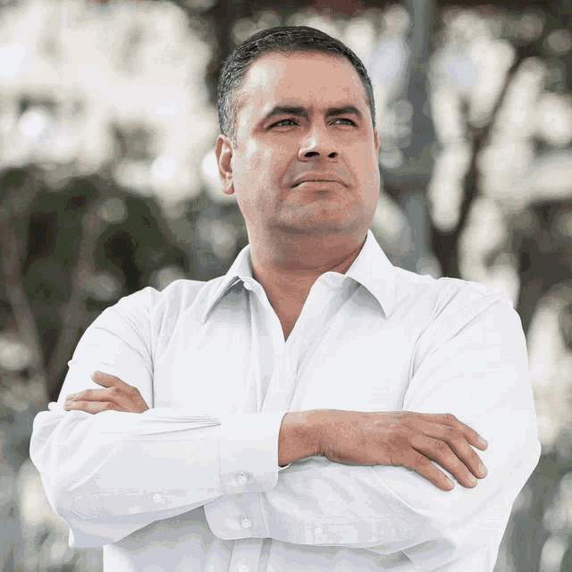 a man in a white shirt with his arms crossed looks to the side