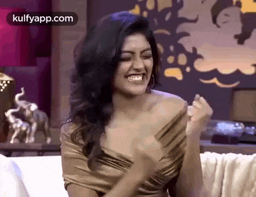 a woman is sitting on a couch with her fist in the air and smiling .