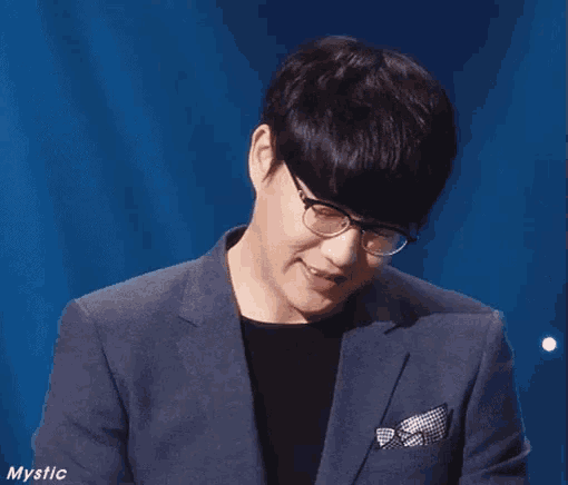a man wearing glasses and a suit is smiling and looking down .
