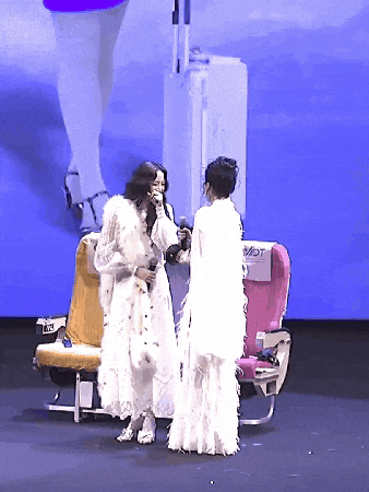 a woman in a white dress stands next to another woman in a white dress in front of an airplane seat that says vat