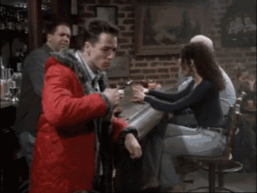 a man in a red jacket is sitting at a bar drinking beer