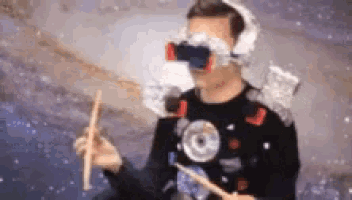 a man is wearing a virtual reality headset and holding a drum stick .