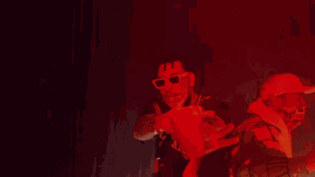 a man wearing sunglasses is standing next to another man in a red light