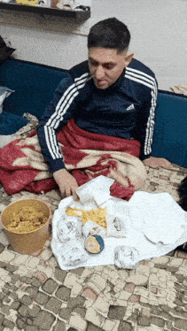 a man wearing an adidas jacket sits on a couch with food