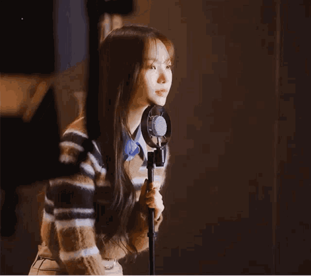 a woman is singing into a microphone while wearing a plaid sweater .