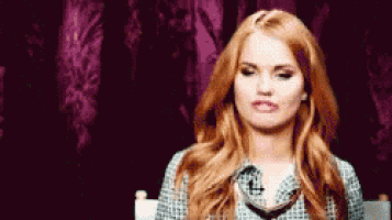 a woman with red hair is sitting in a chair with her eyes closed and making a funny face .