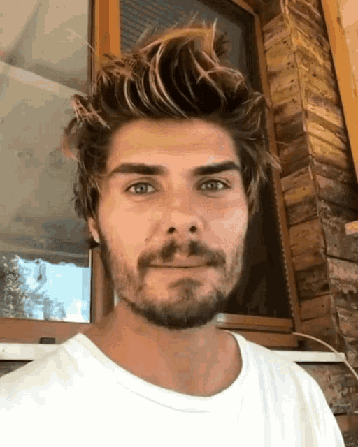 a man with a beard wearing a white shirt looks at the camera