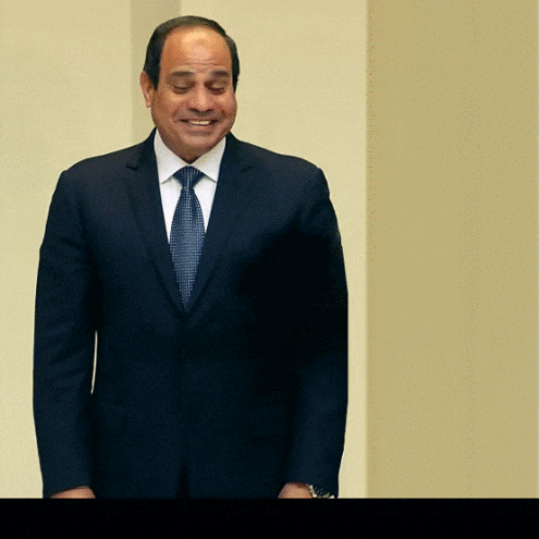 a man in a suit and tie smiles while standing in front of a wall