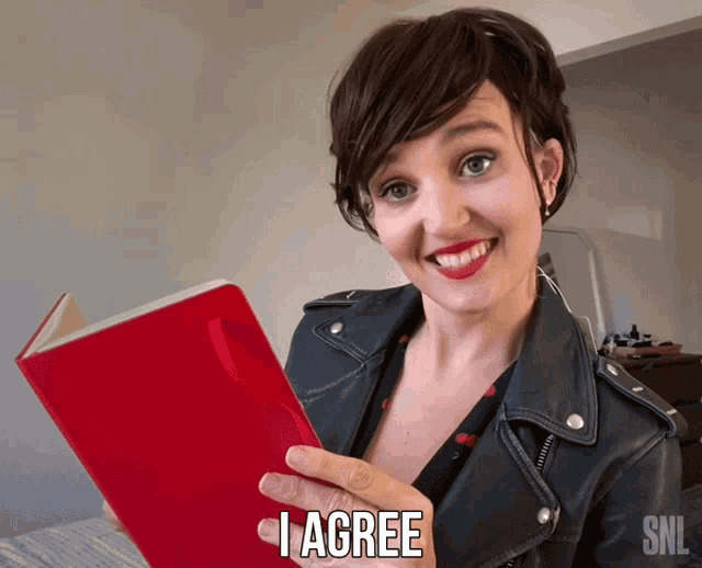 a woman in a leather jacket is holding a red book that says i agree on it
