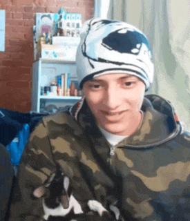 a man wearing a camouflage jacket and a beanie is holding a cat in his arms