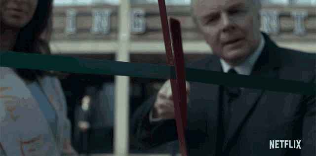 a man in a suit is cutting a red ribbon in front of a building that says ing on it
