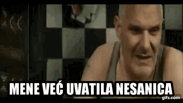 a bald man in a tank top is sitting in front of a checkered tile wall .