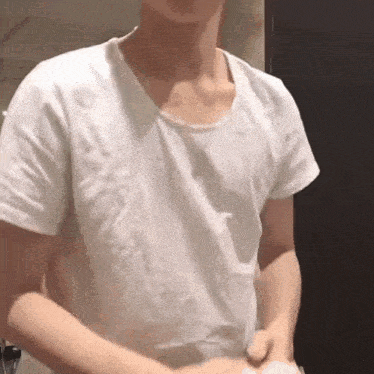 a man in a white t-shirt is standing in a bathroom .