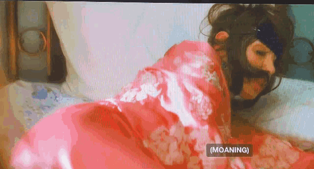a woman in a pink robe is laying on a bed with a sign that says moaning on it