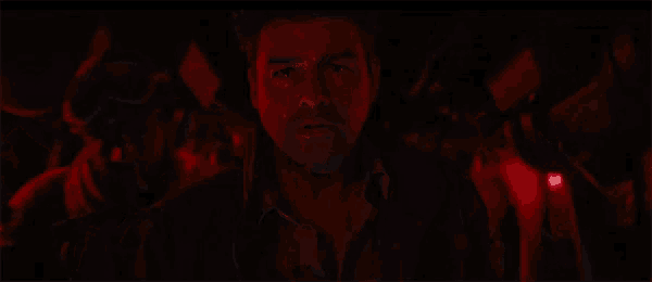 a close up of a man 's face in a dark room with a red light behind him