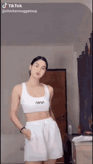 a woman wearing a white crop top and white shorts is standing in a room .