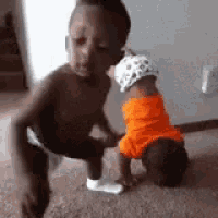 a little boy kneeling down next to a baby wearing an orange shirt .